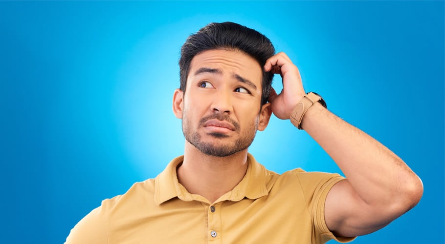 A man wearing a yellow polo shirt scratches his head and looks uncertain against a blue background.