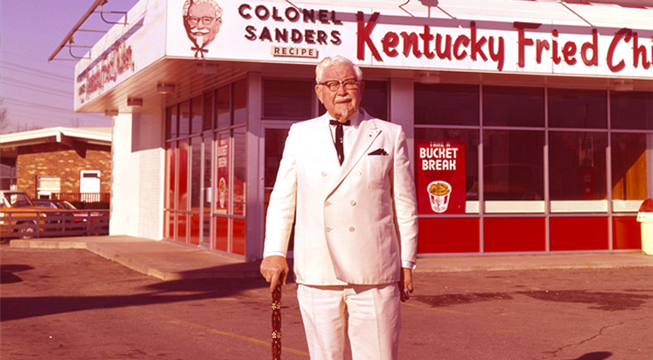 Colonel Sanders standing in front of KFC