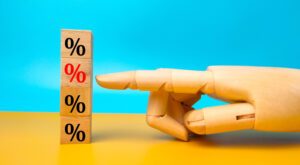 A wooden mannequin hand points at stacked wooden blocks marked with percentage symbols against a bright teal and yellow background.